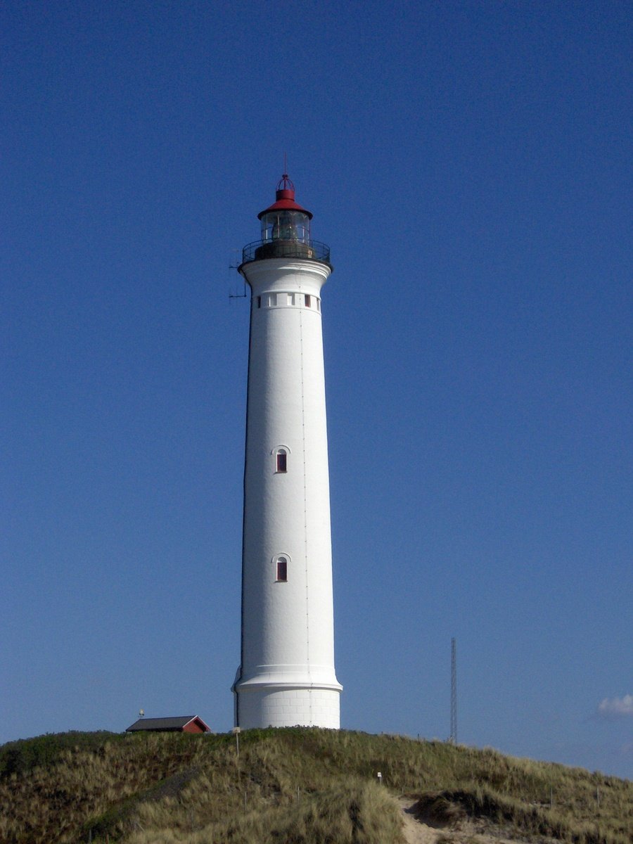 a white lighthouse on top of a hill under a blue sky