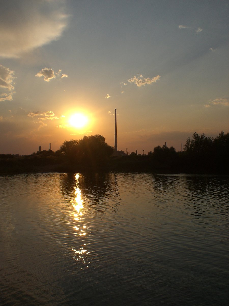 the sun sets over the horizon at a river in a city