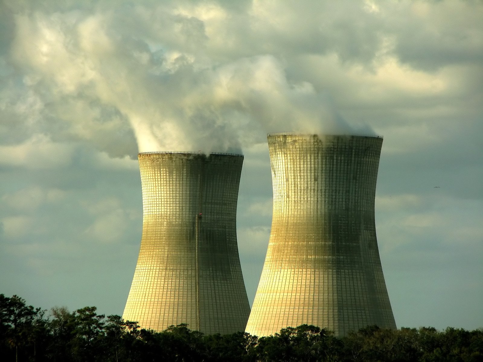 two cooling towers with black smoke and green trees