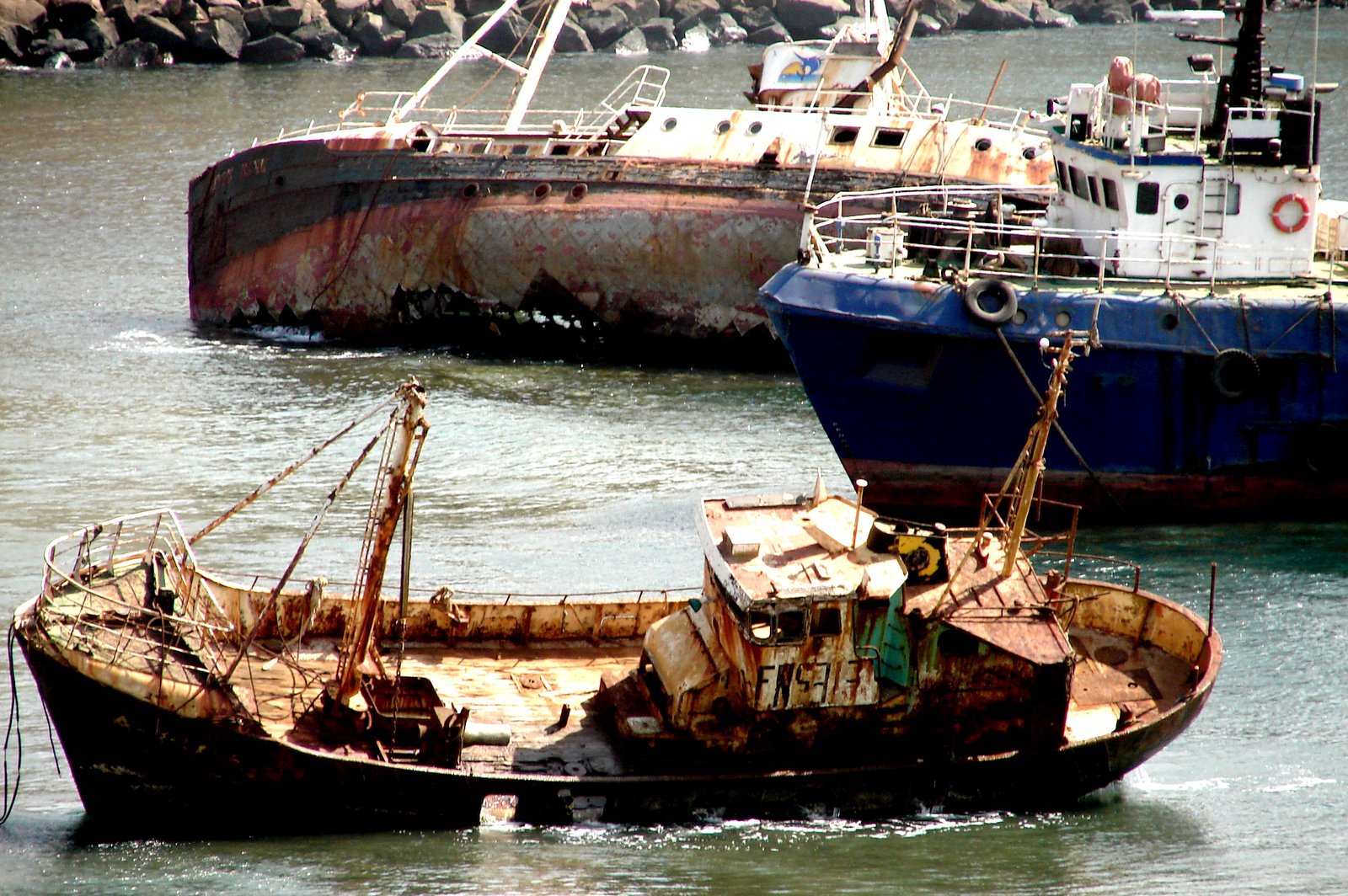 two rusted ships in the water with a rocky shore