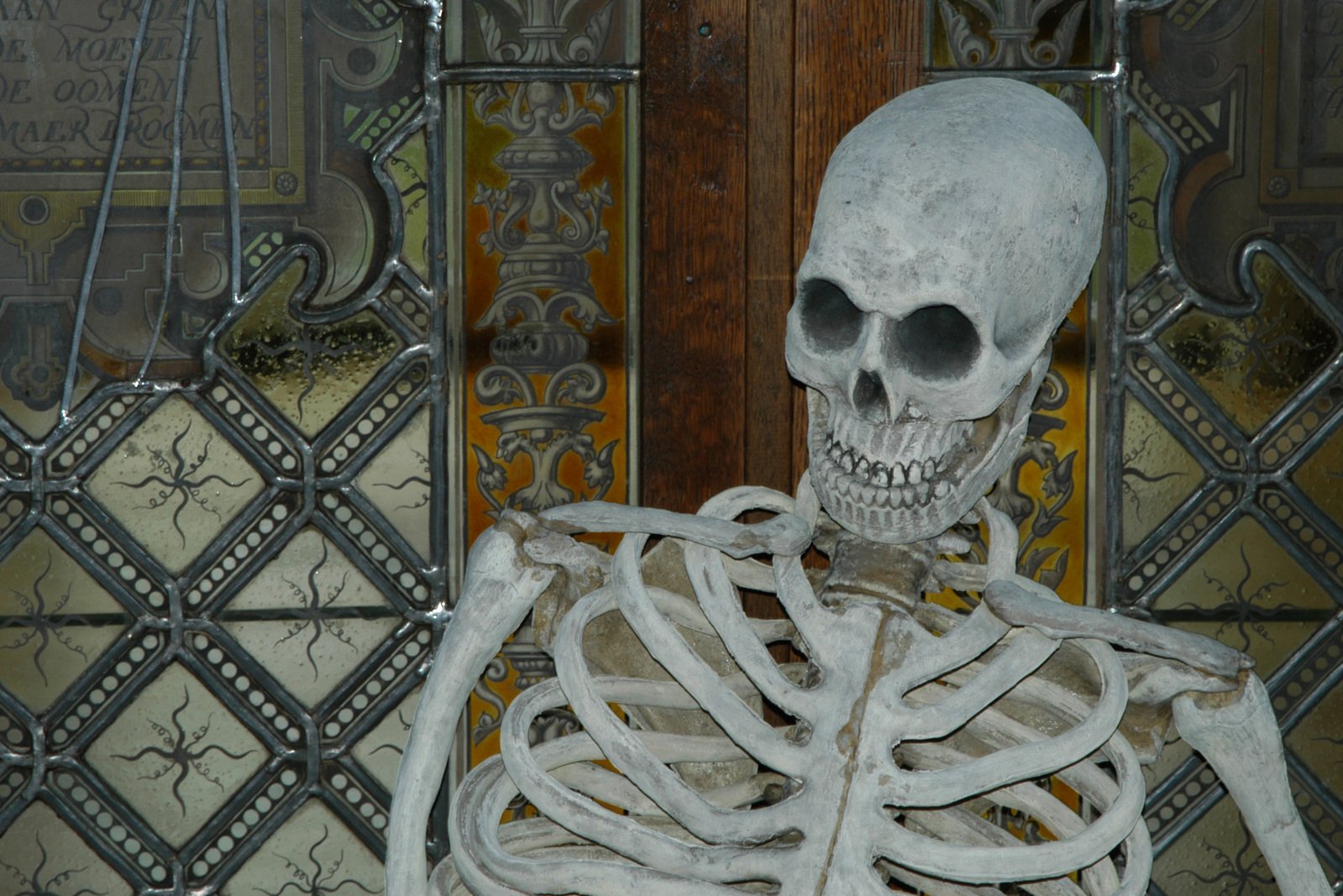 a skeleton sitting in front of a large metal gate