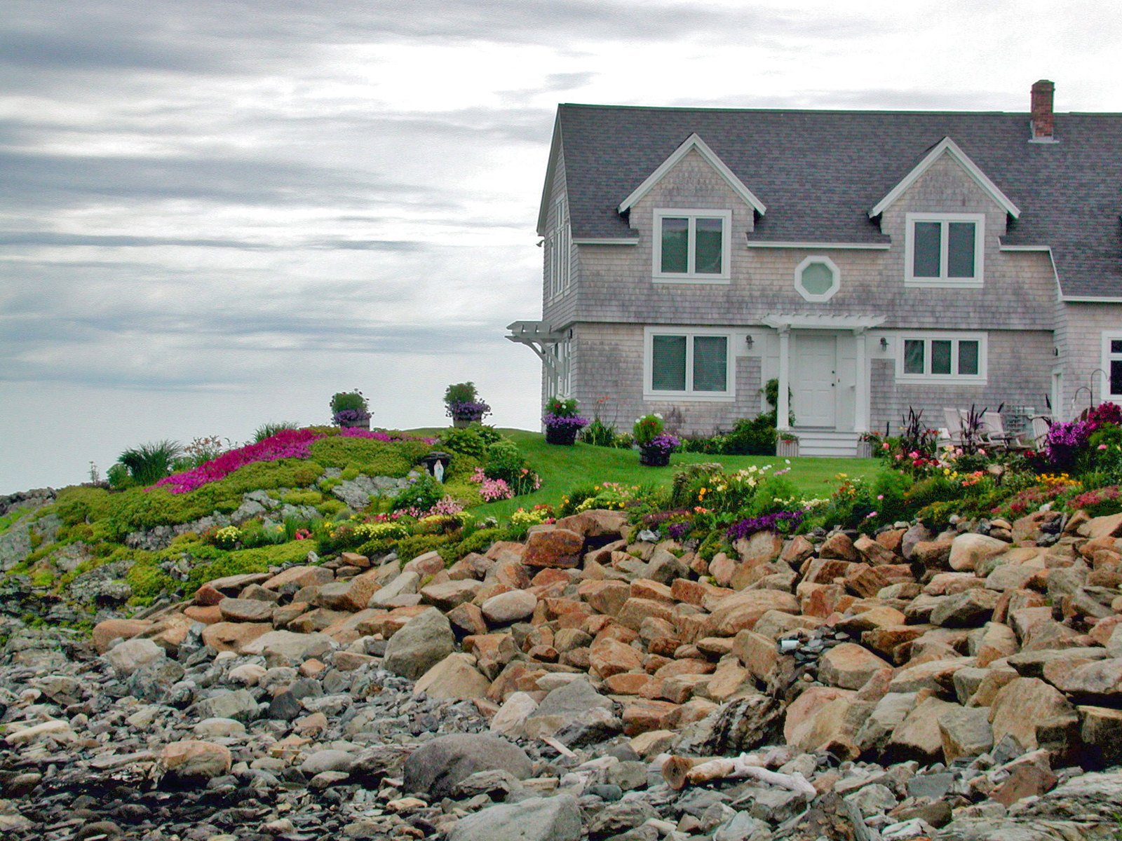 a large house next to some rocks and purple flowers