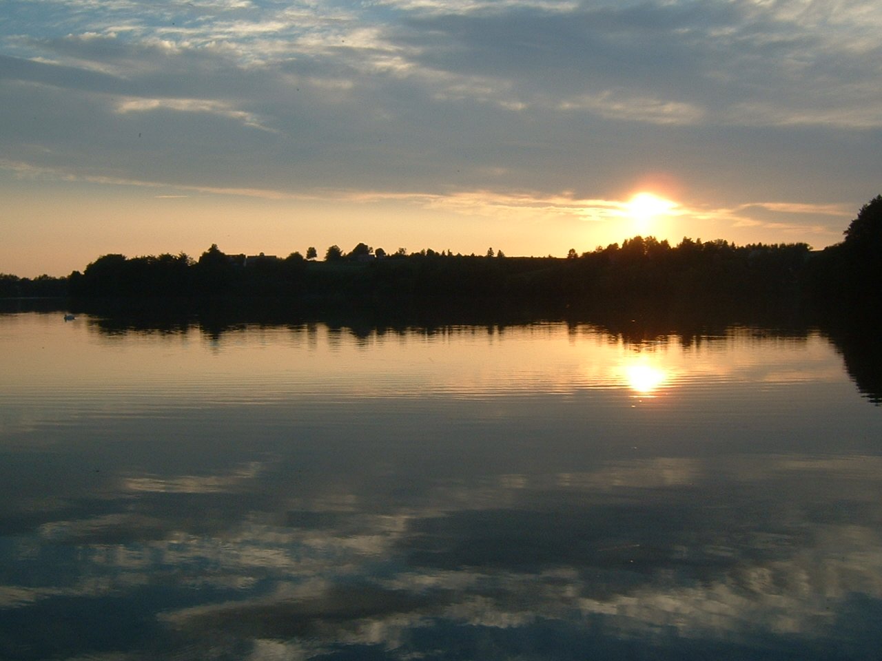 the sun is rising on a calm, still lake