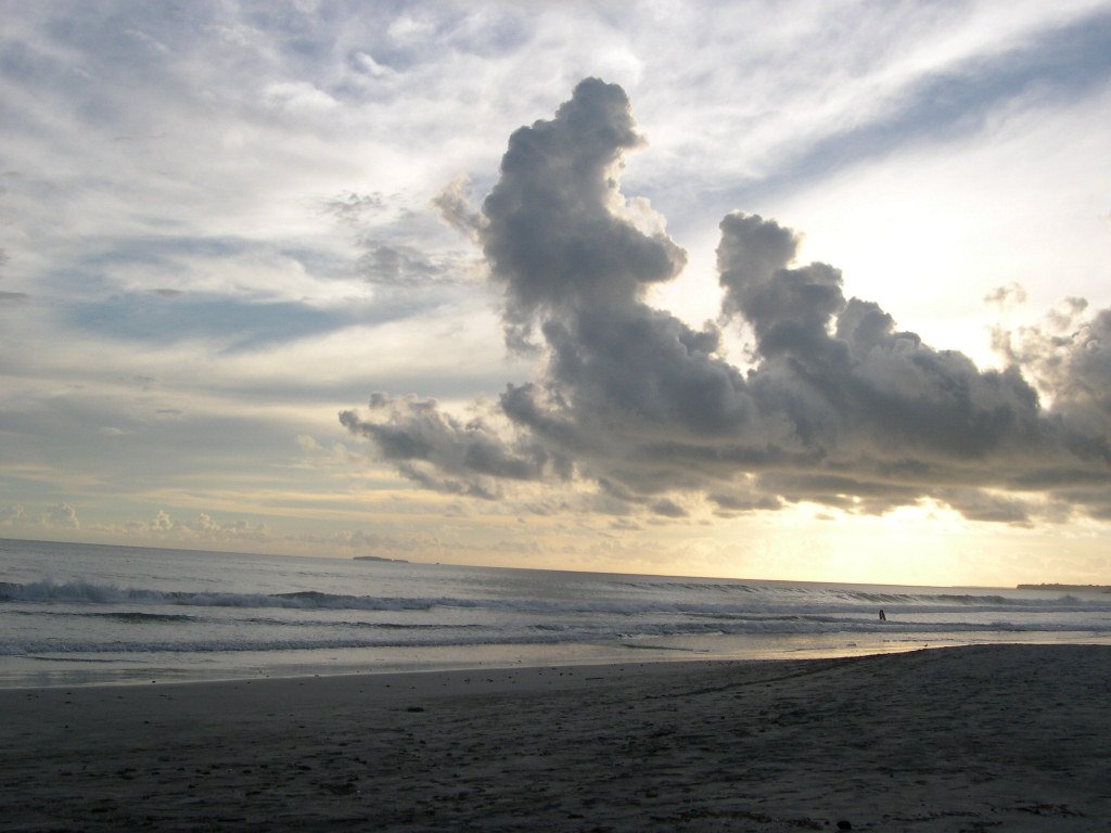 a man in silhouette standing at the beach with waves coming toward him