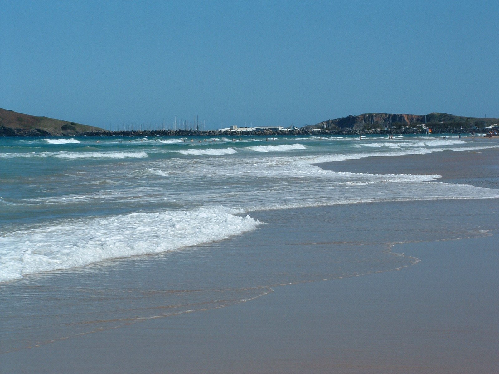 a person stands in the surf on a beach near small buildings