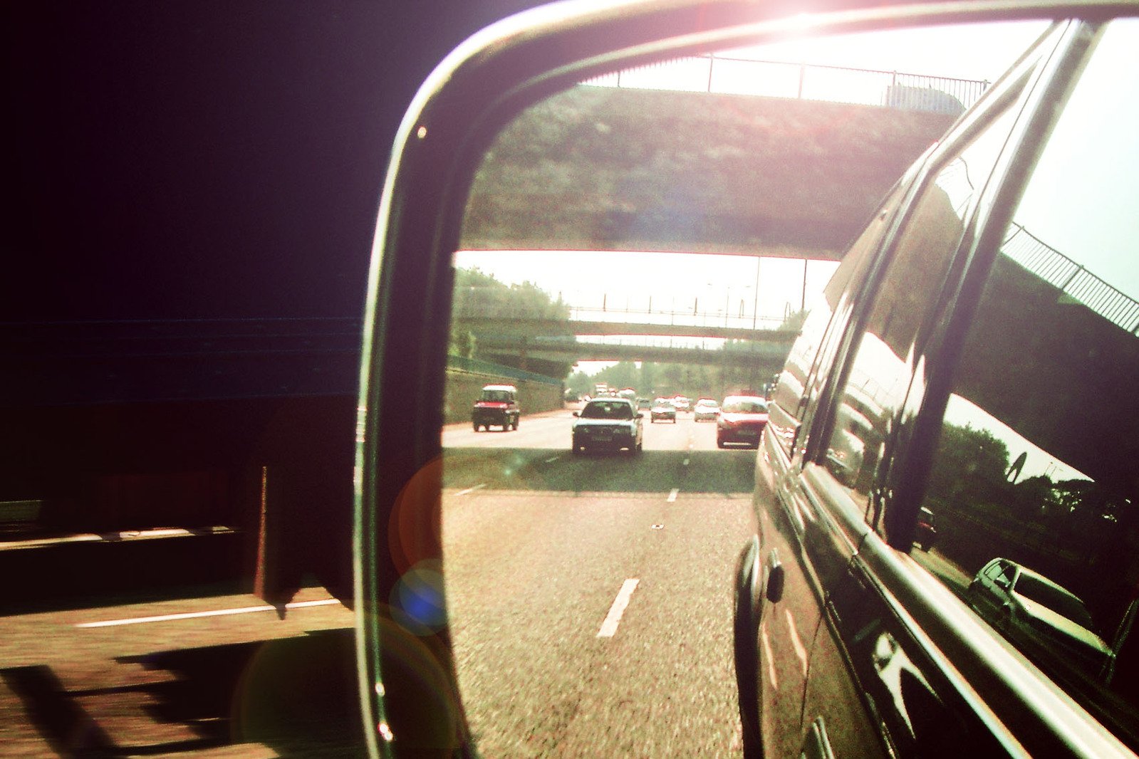 the view out a car's side mirror with another car driving under a bridge