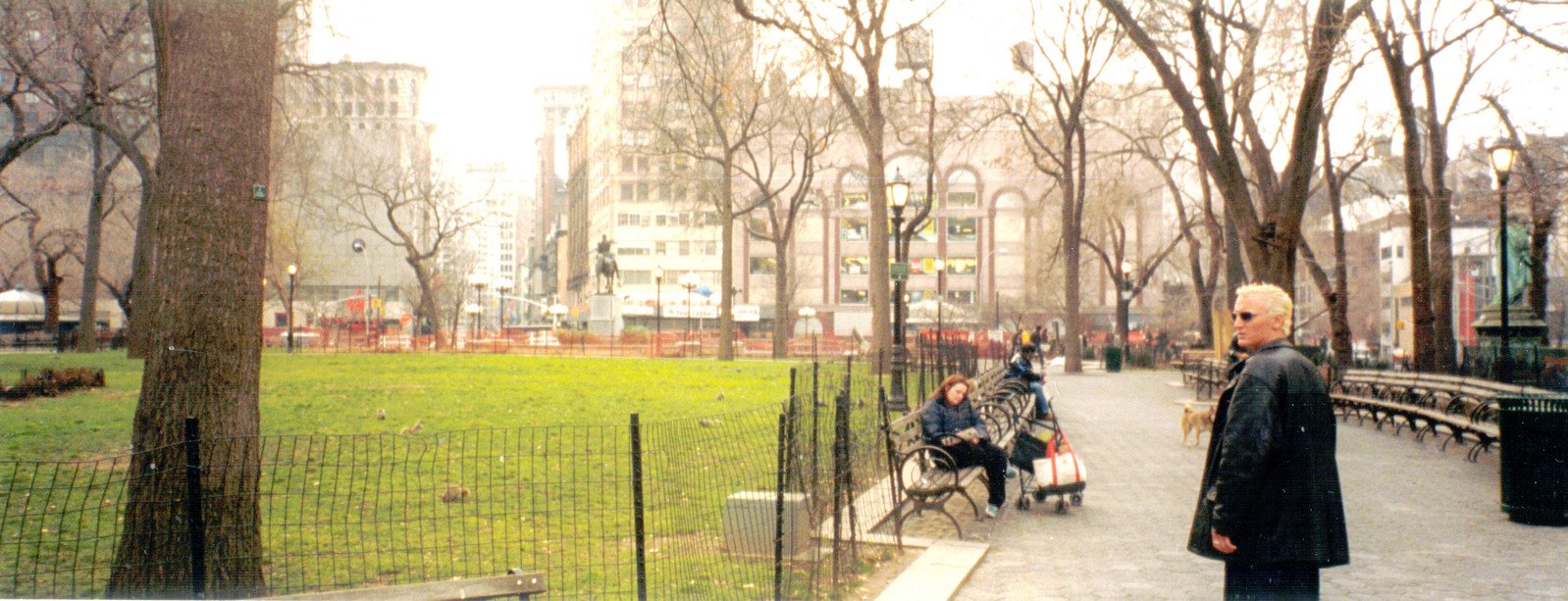 a park with several people sitting on benches and a grassy area