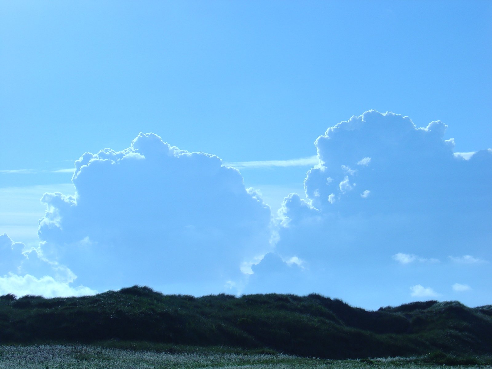 large fluffy white clouds float in the blue sky above green hills