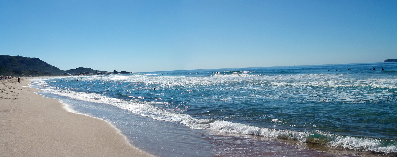 several people are walking along a beach by the water