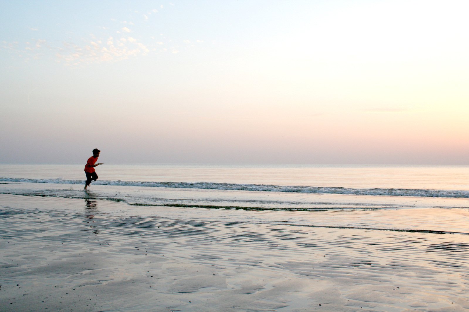 man in red running on the shore as the sun sets