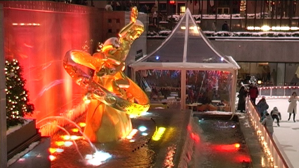 people on an ice rink skating around an elaborate fountain