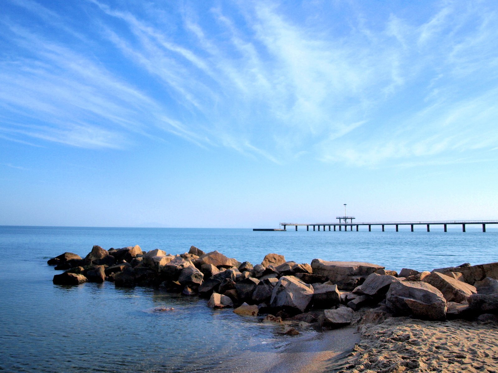 a view of a pier across the water from rocks