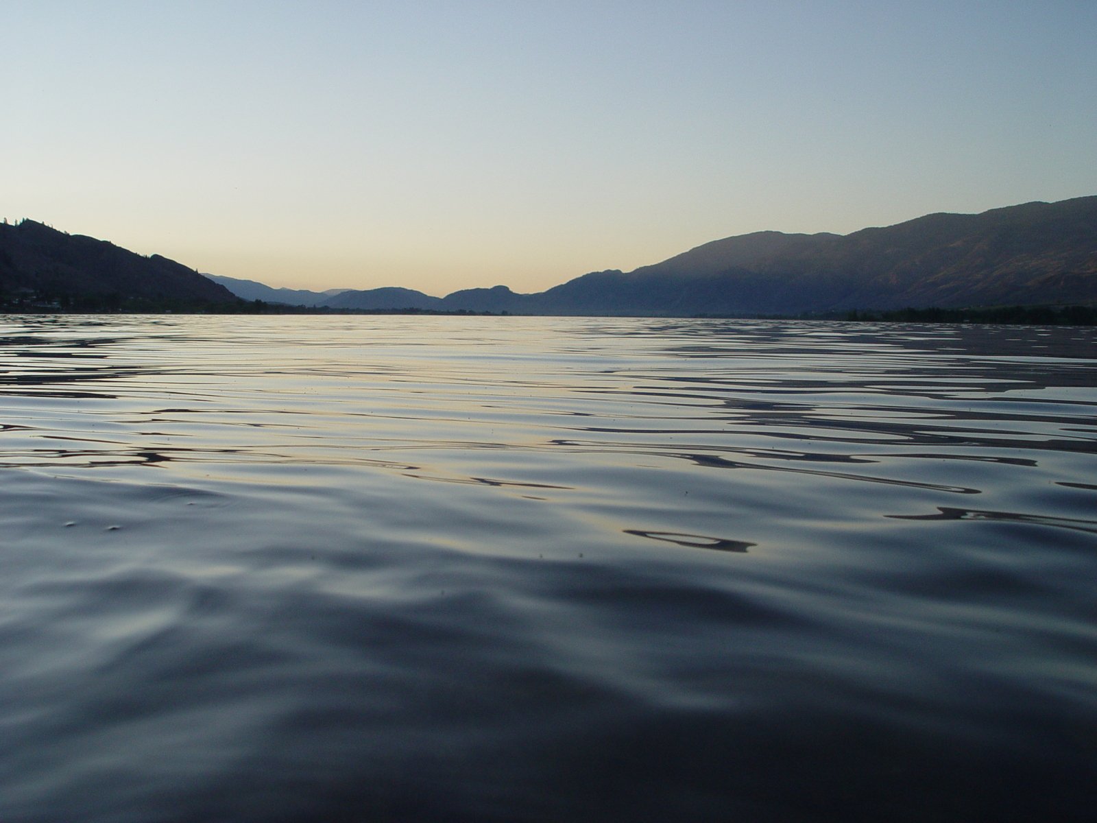 some small waves on the water with mountains in the background