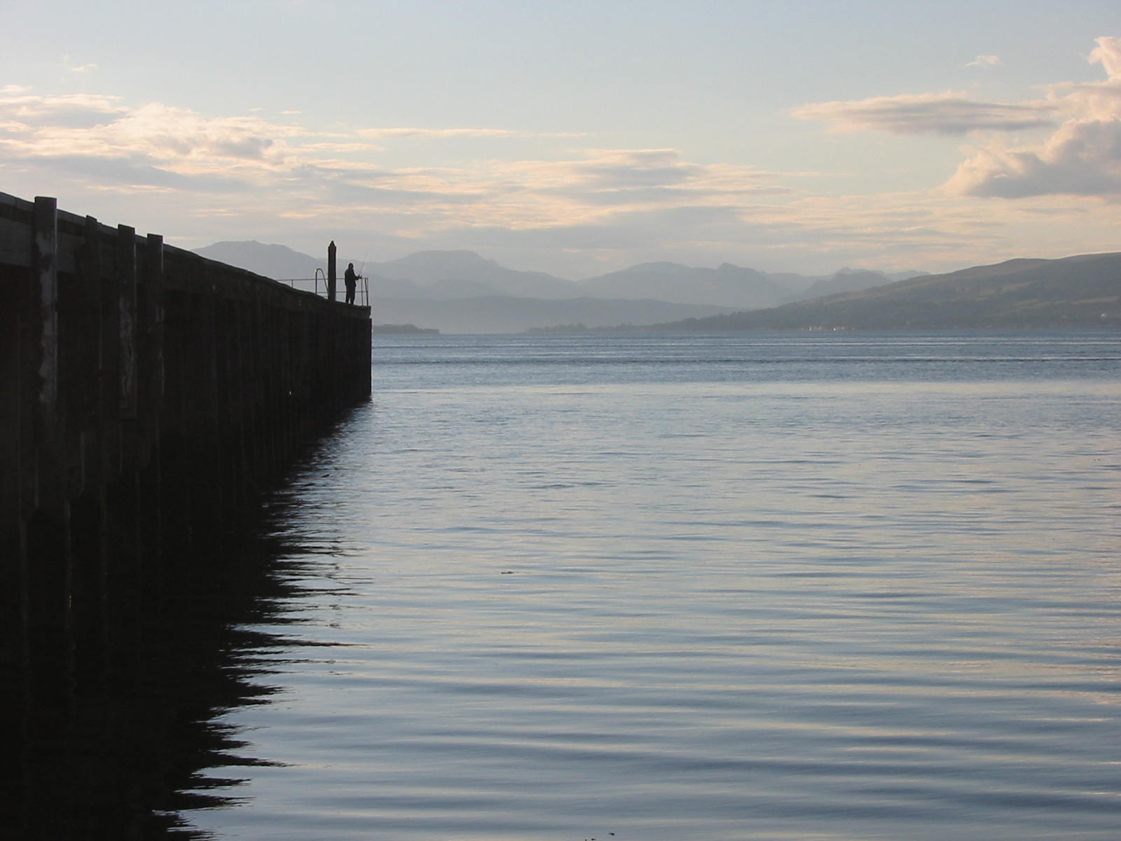 two people stand on the side of a pier next to the water