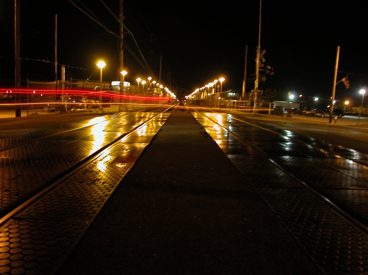 a dark city street at night time with street lights and street lights reflecting off wet pavement