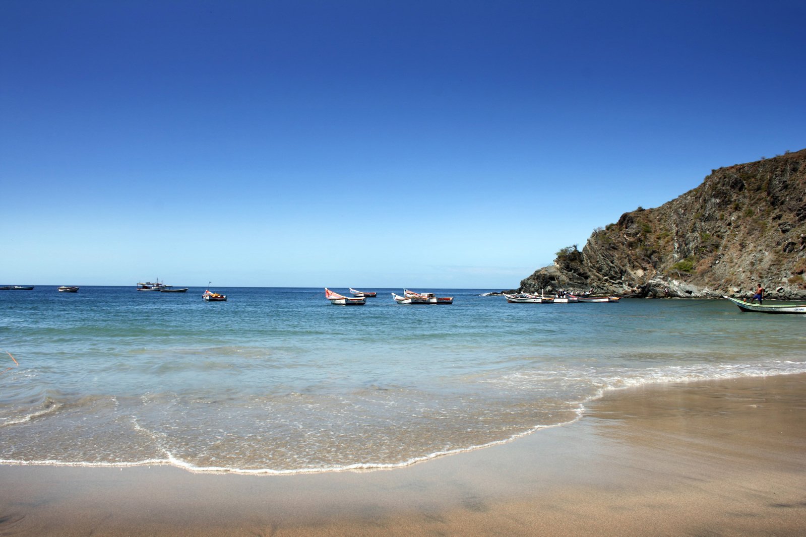 a view of several small boats in the water near a beach