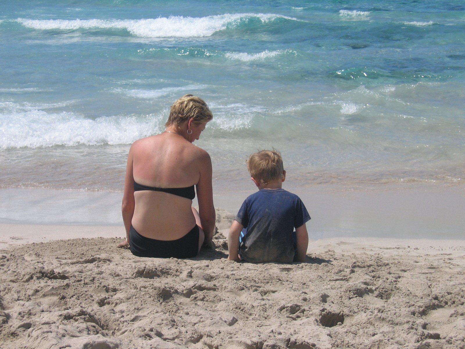 a woman sitting on top of a sandy beach next to a child