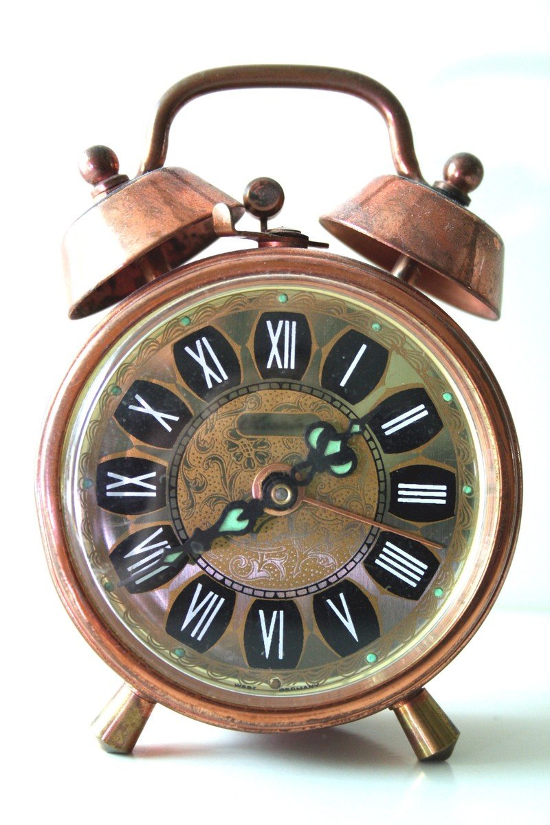 an old vintage copper alarm clock with a small bell sitting on a stand