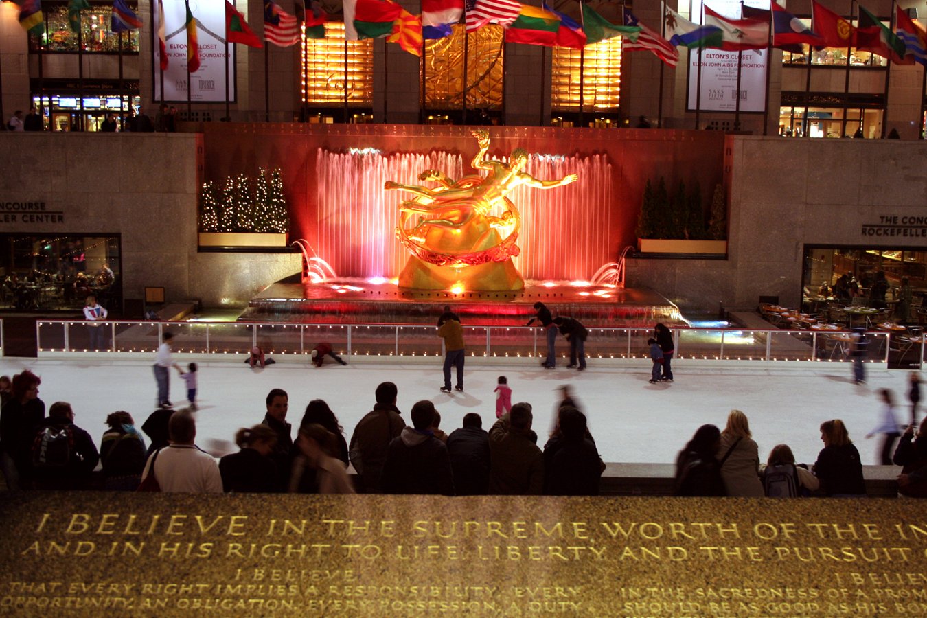 a group of people standing around a fountain with a large statue on it's side