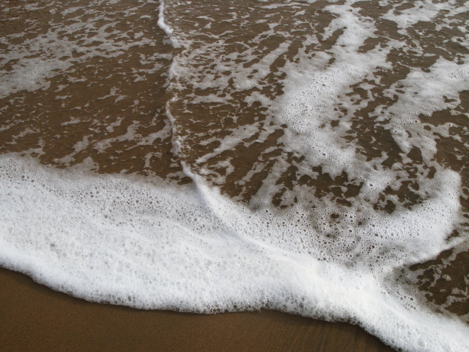a wave coming in to the shore with white foam