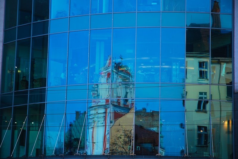 the clock tower is reflected in the windows of a modern building