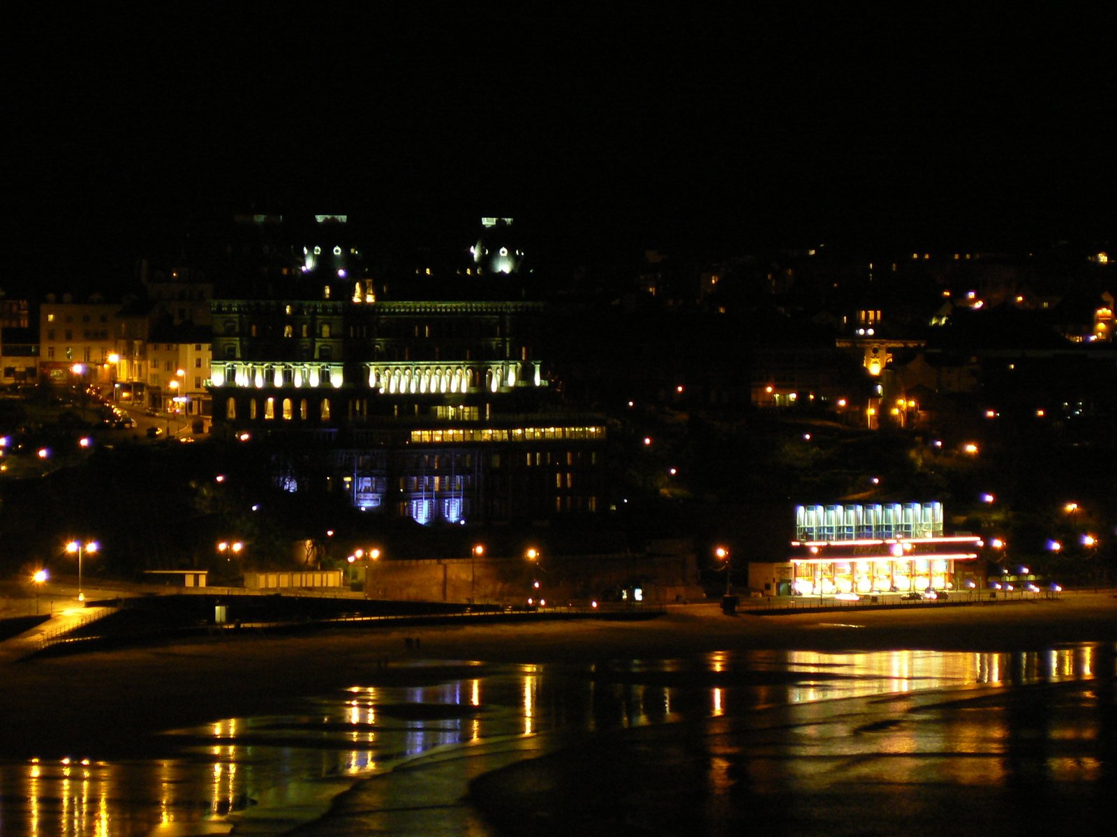 the buildings are lit up at night beside the water