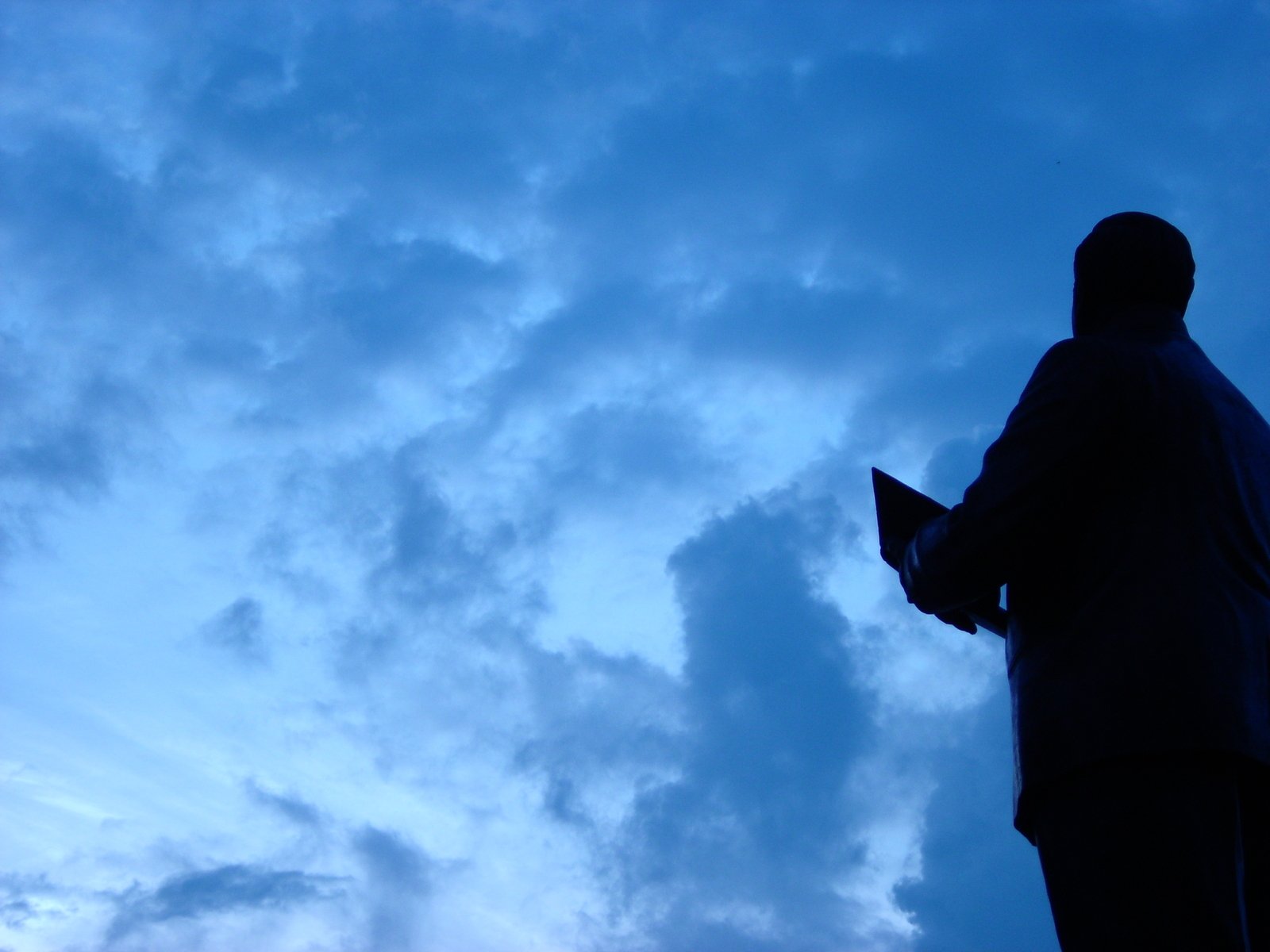 a silhouette of a man holding a laptop in front of the clouds