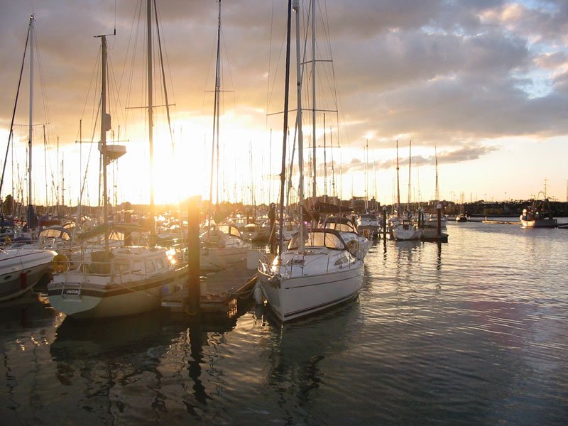 the sun is setting on many sailboats docked at a marina