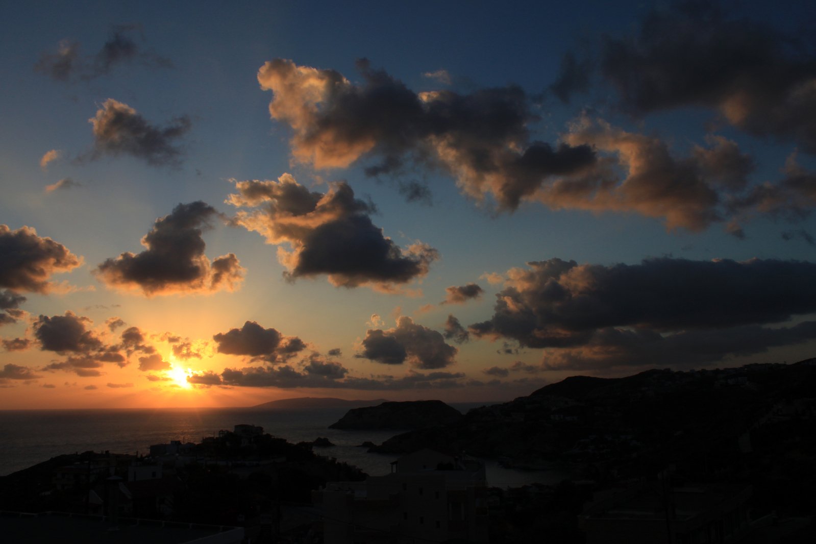 sun sets over an ocean with fluffy clouds and small islands