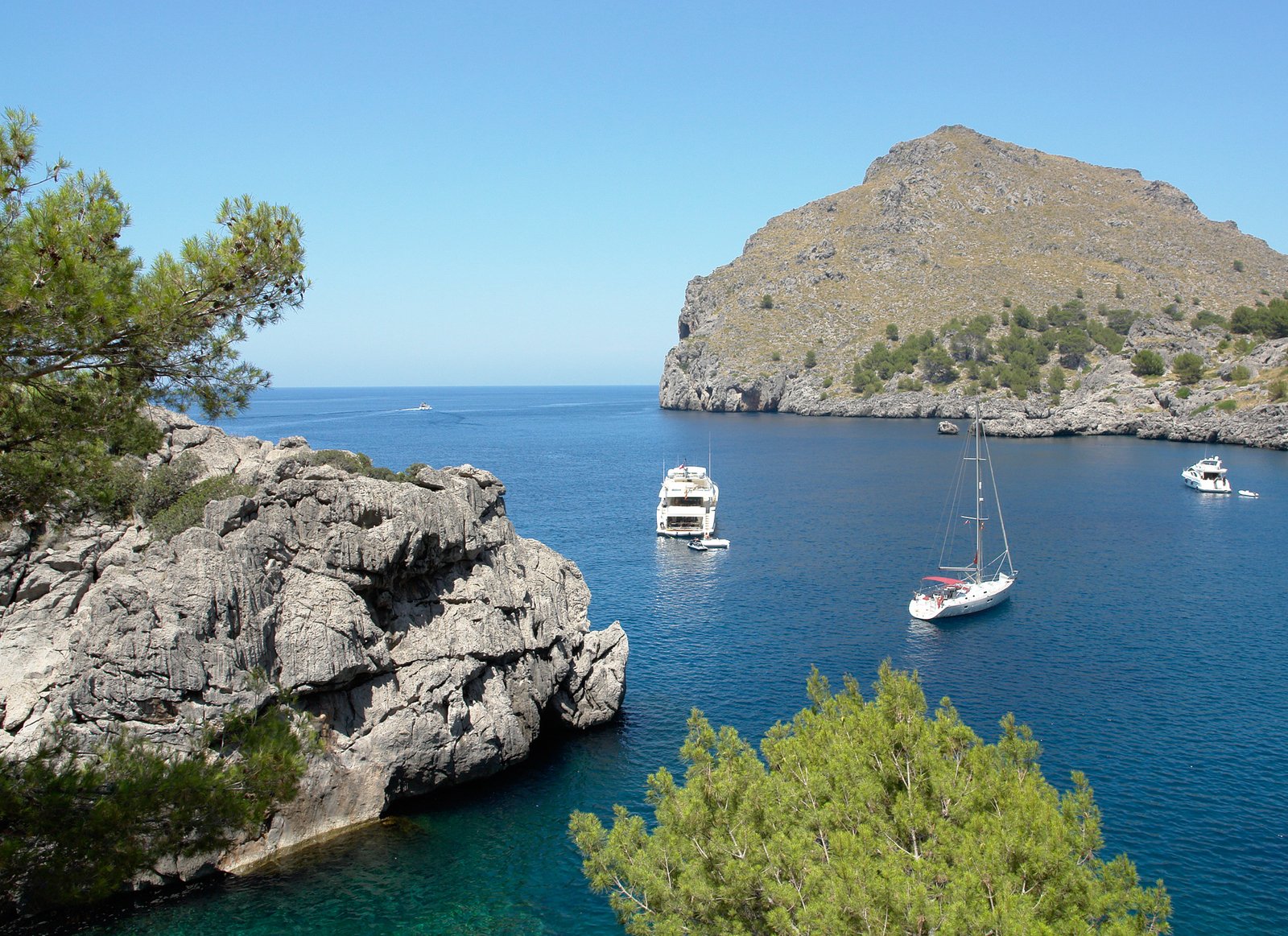 three boats in the open water near a rocky shoreline