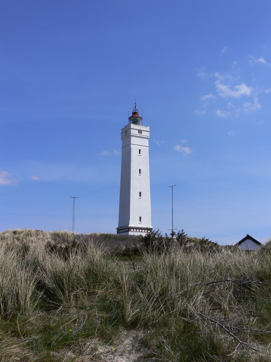 a white lighthouse on top of a grassy hill