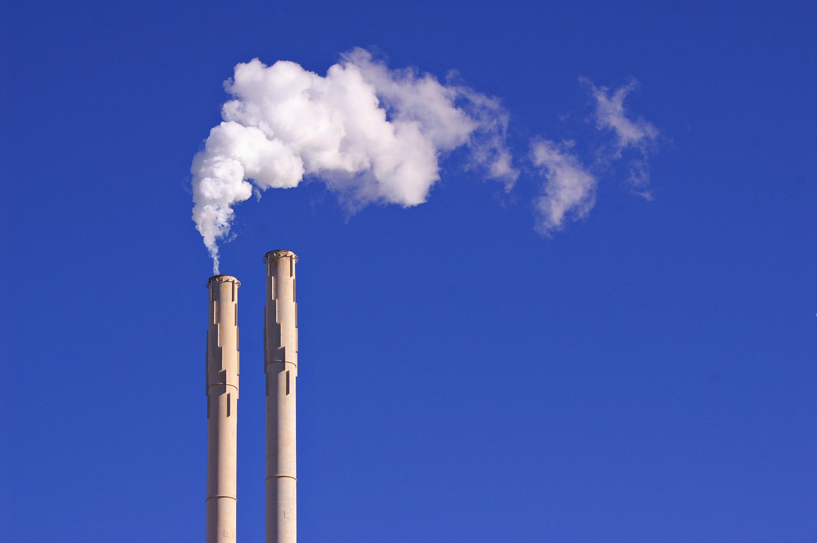 smoke comes out of a factory pipes with bright blue skies in the background