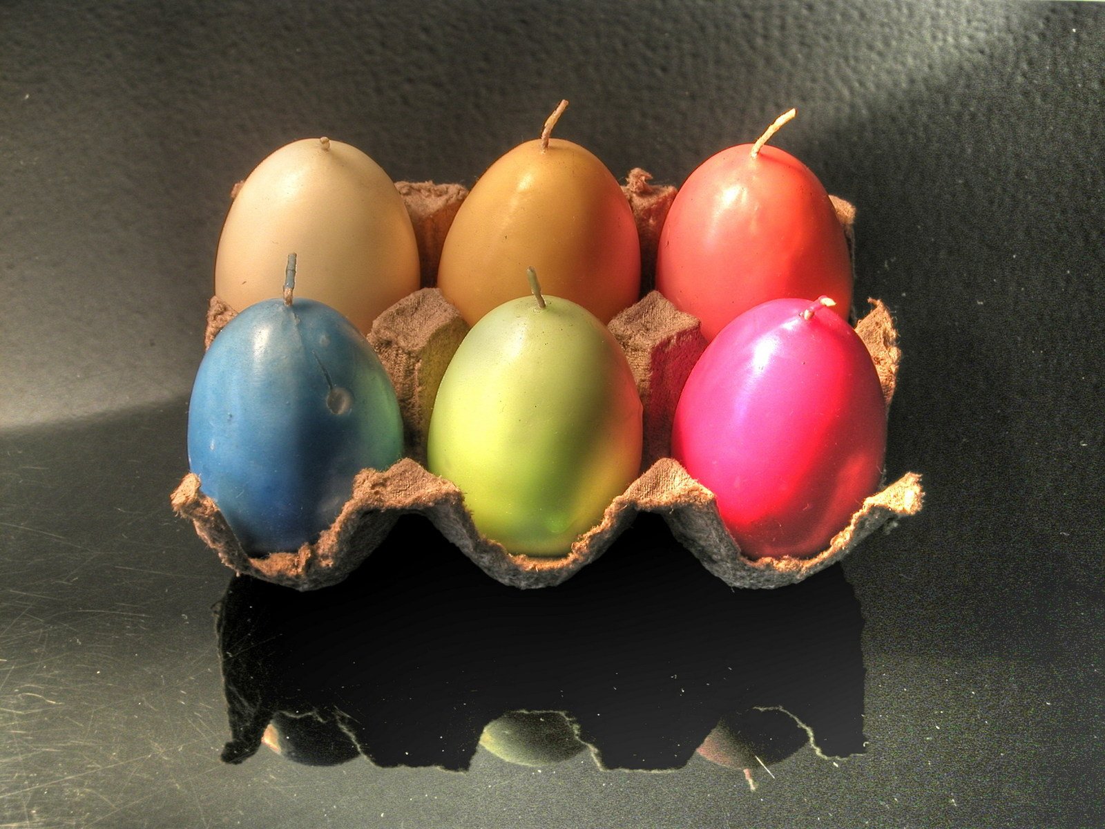 six colored eggs in an egg carton on a table