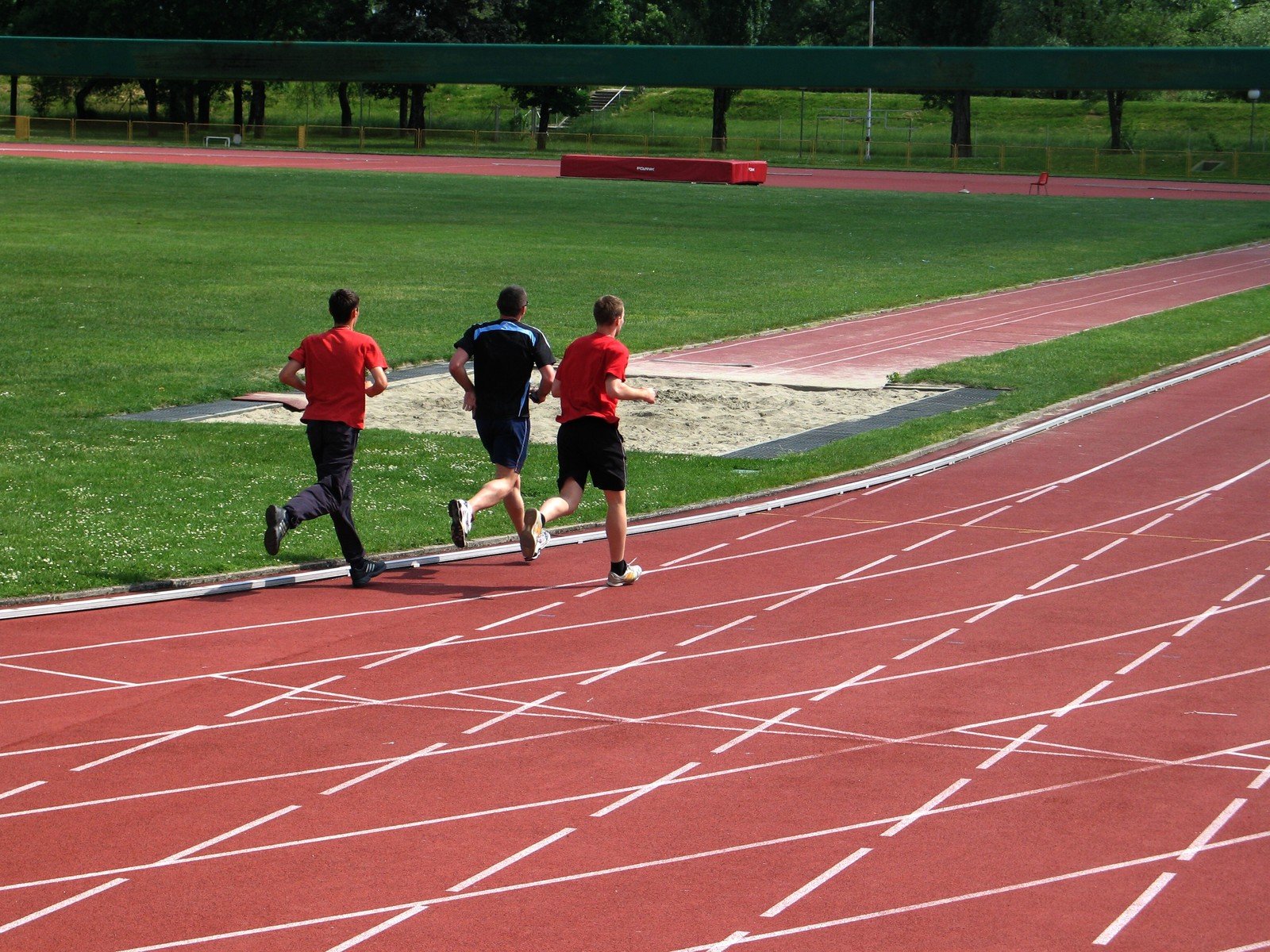 three people running a track next to a field