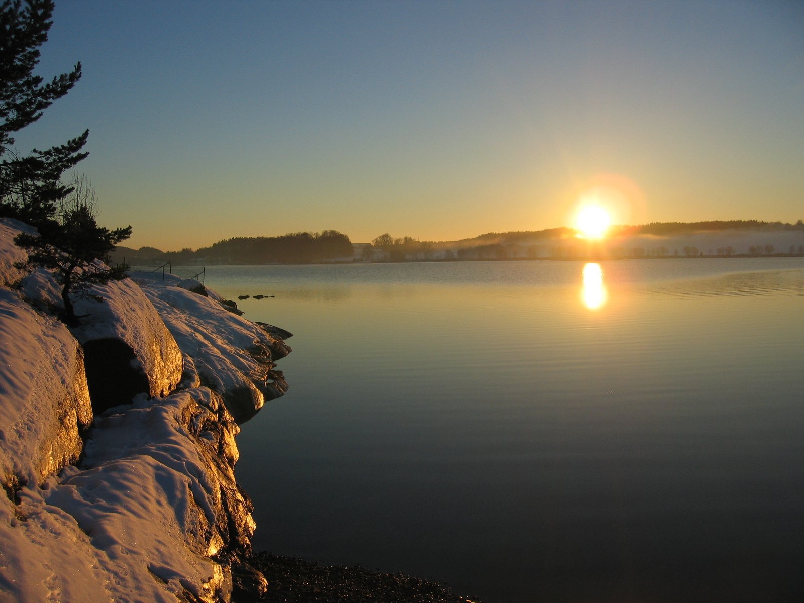 the sun rising over the lake in a wintery landscape