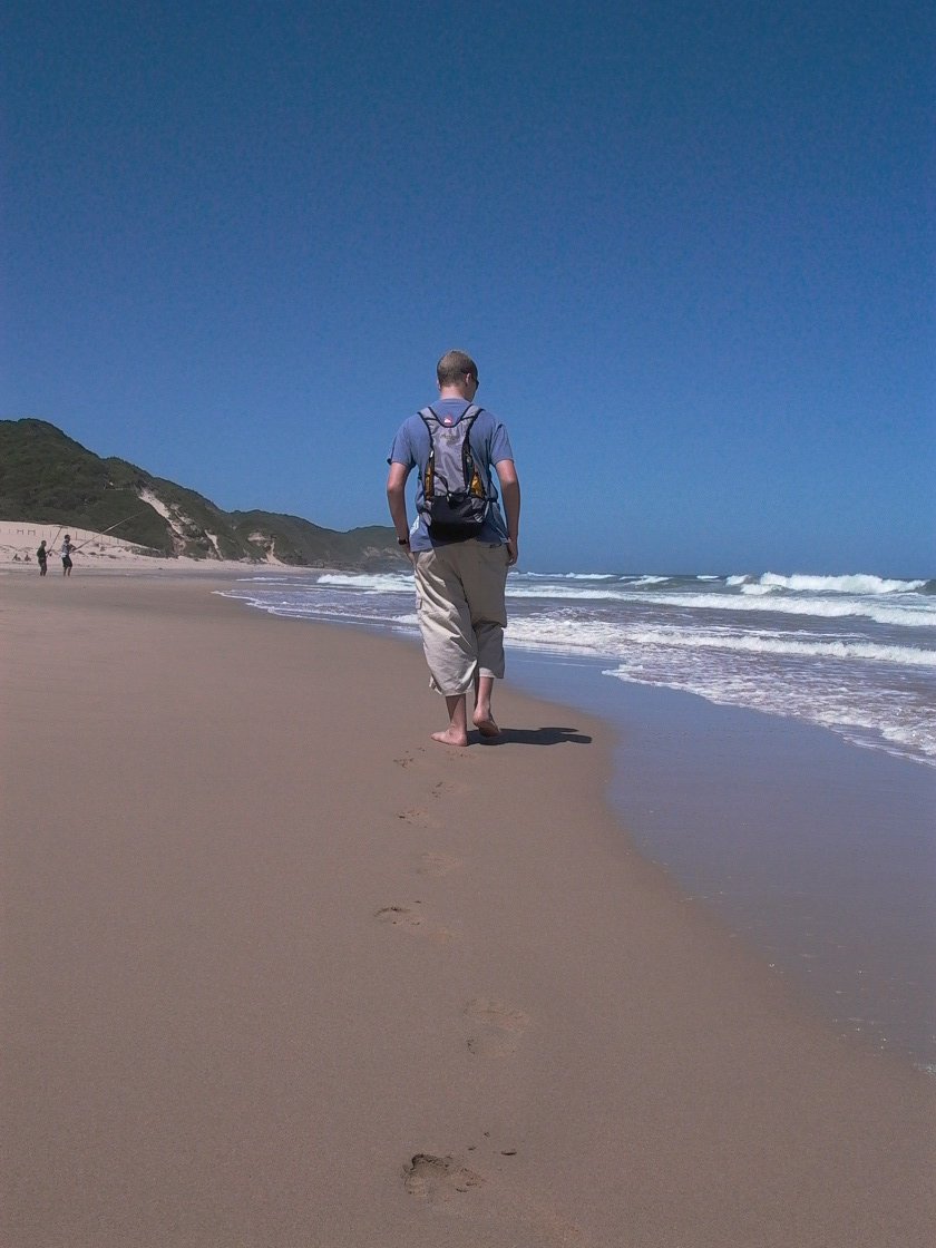 a man walking along the sand toward the ocean