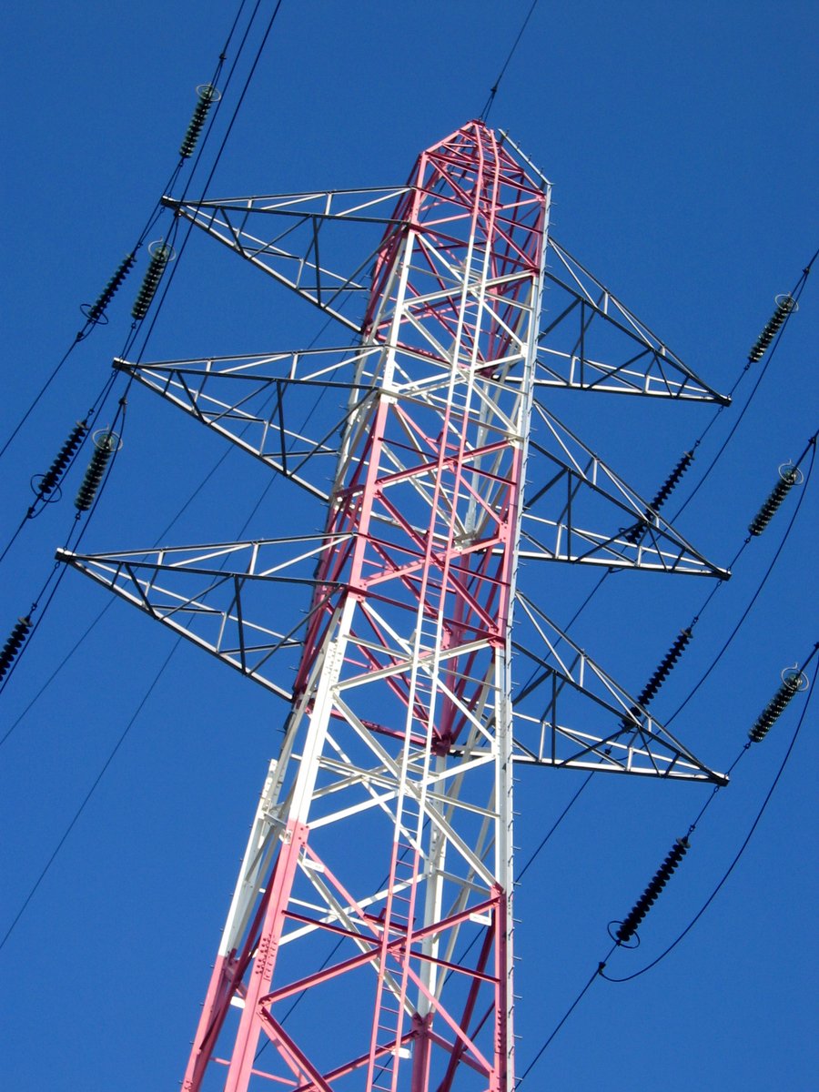 a red and white tower and wires against a blue sky