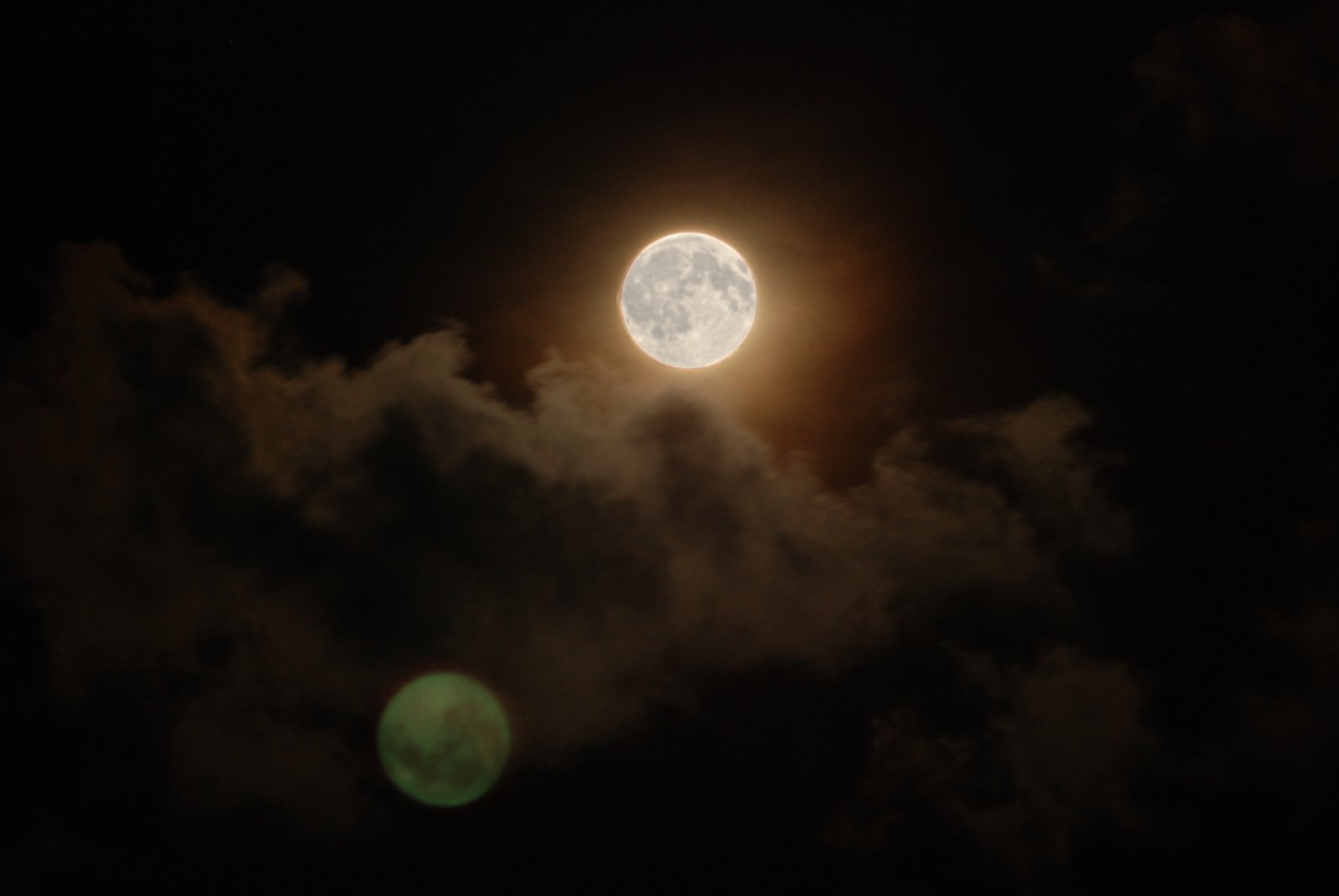 a full moon is seen in the dark sky above clouds