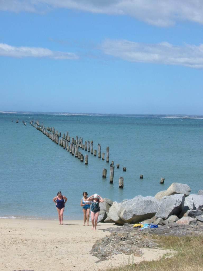 two people walking along the beach while one person takes pictures