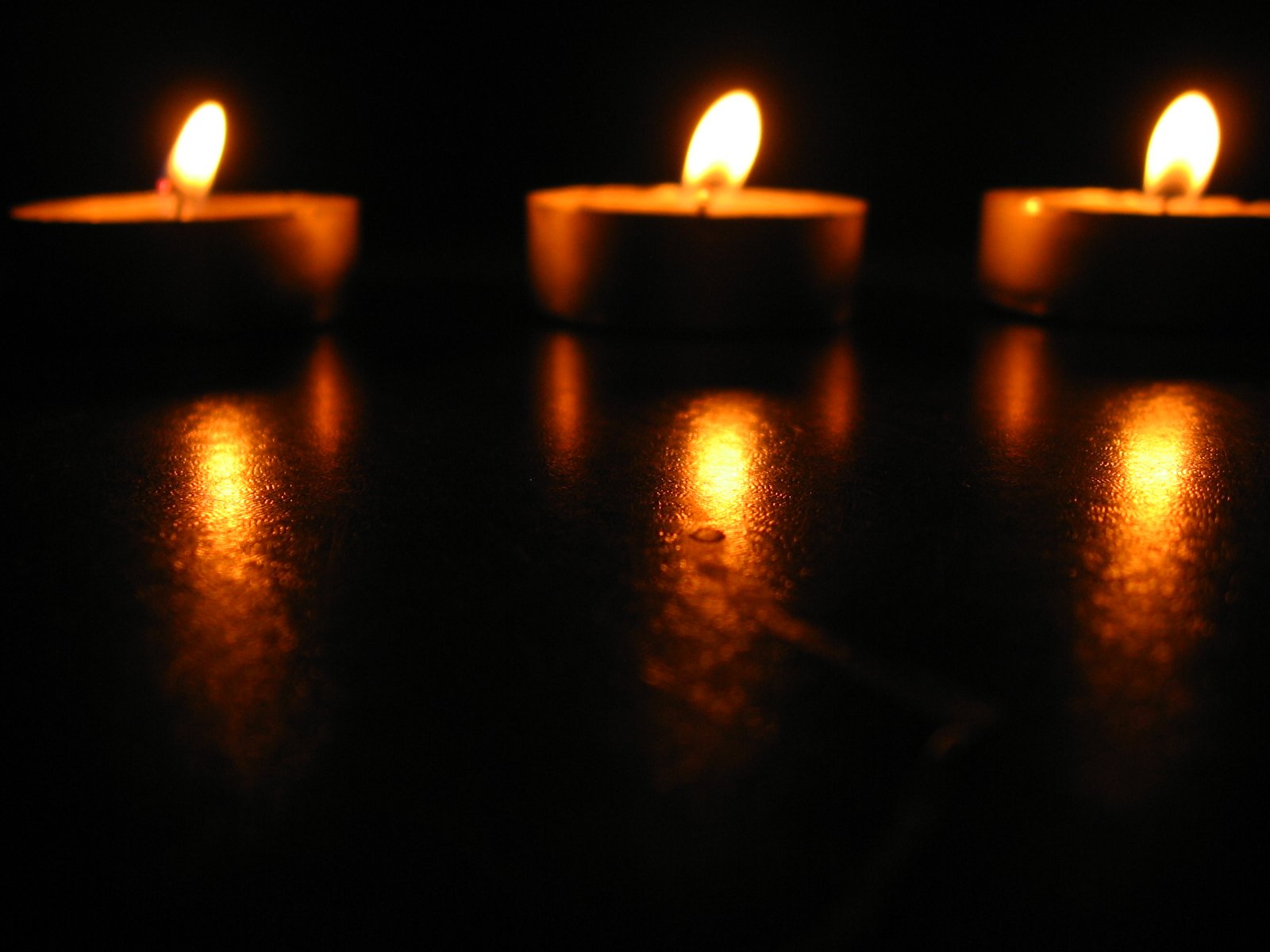 three lit candles with yellow streaks on black