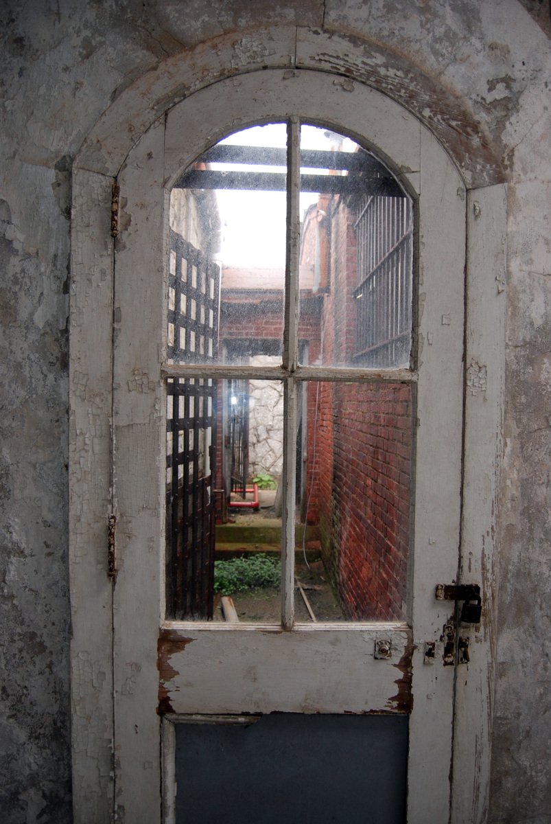the door in the room has a window that reveals an area with bricks, dirt and bricks