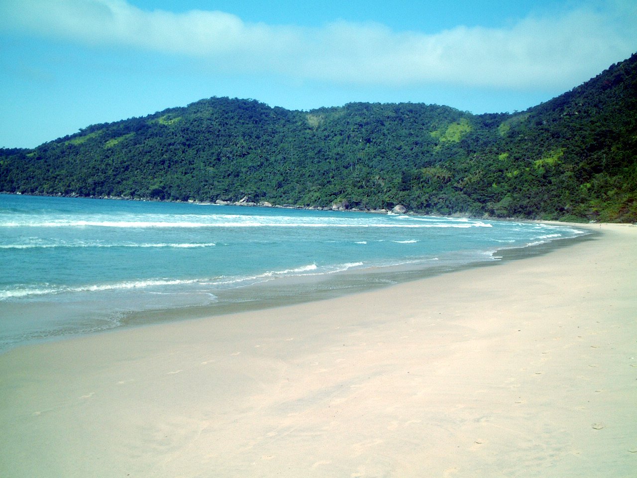 a sandy beach with white sand and green mountains