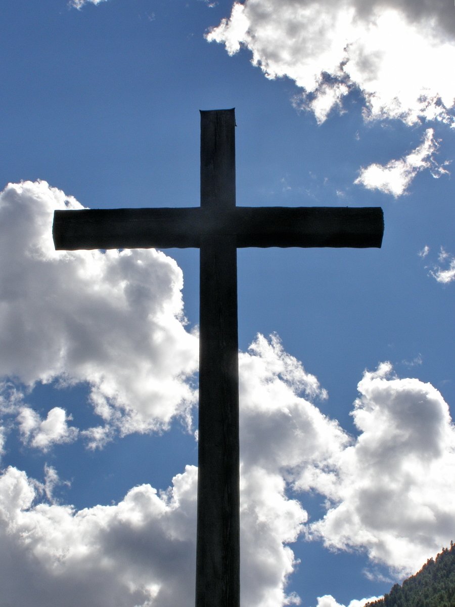 a wooden cross stands tall in front of the clouds