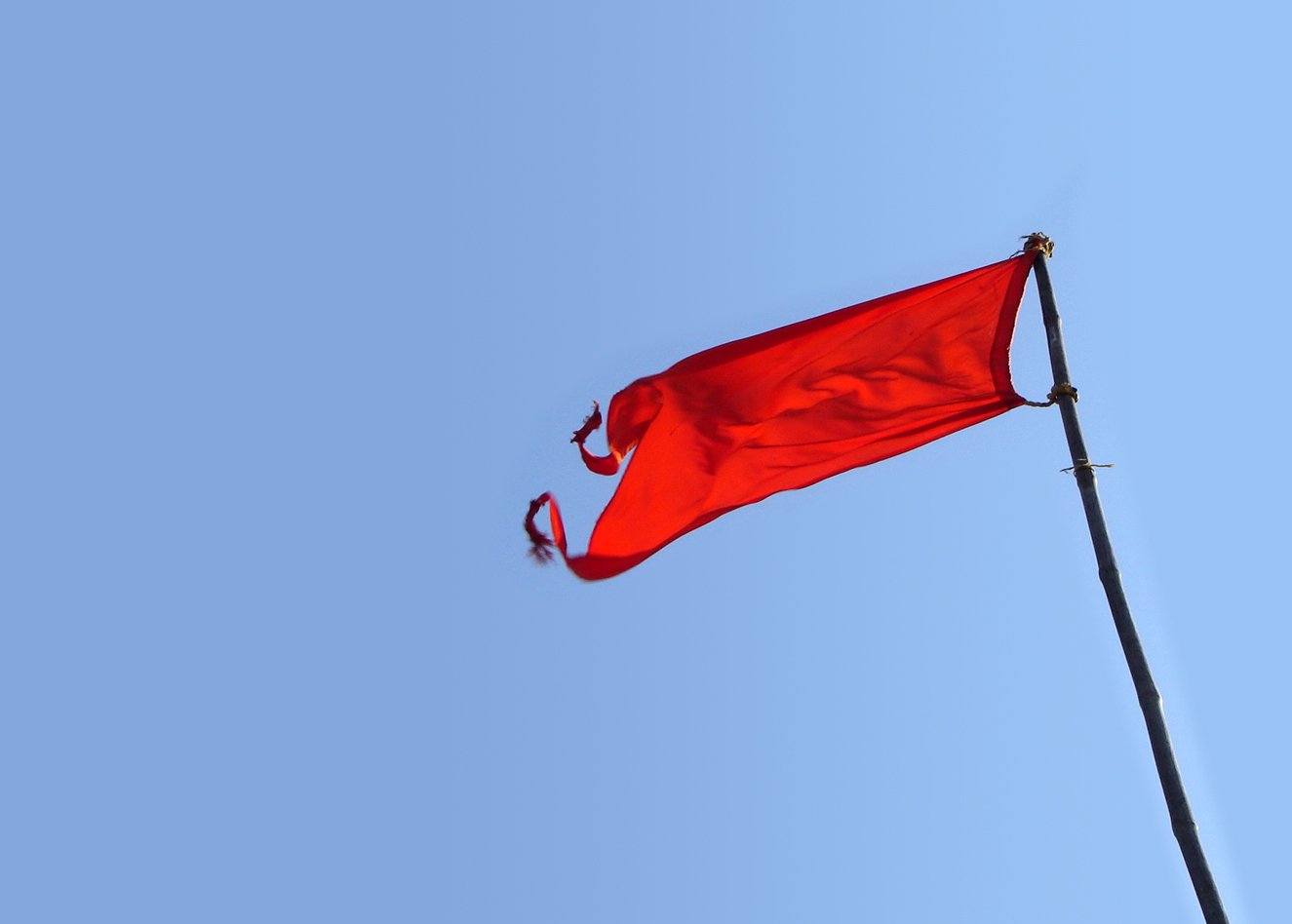 a red flag flying from a pole on top of a blue sky