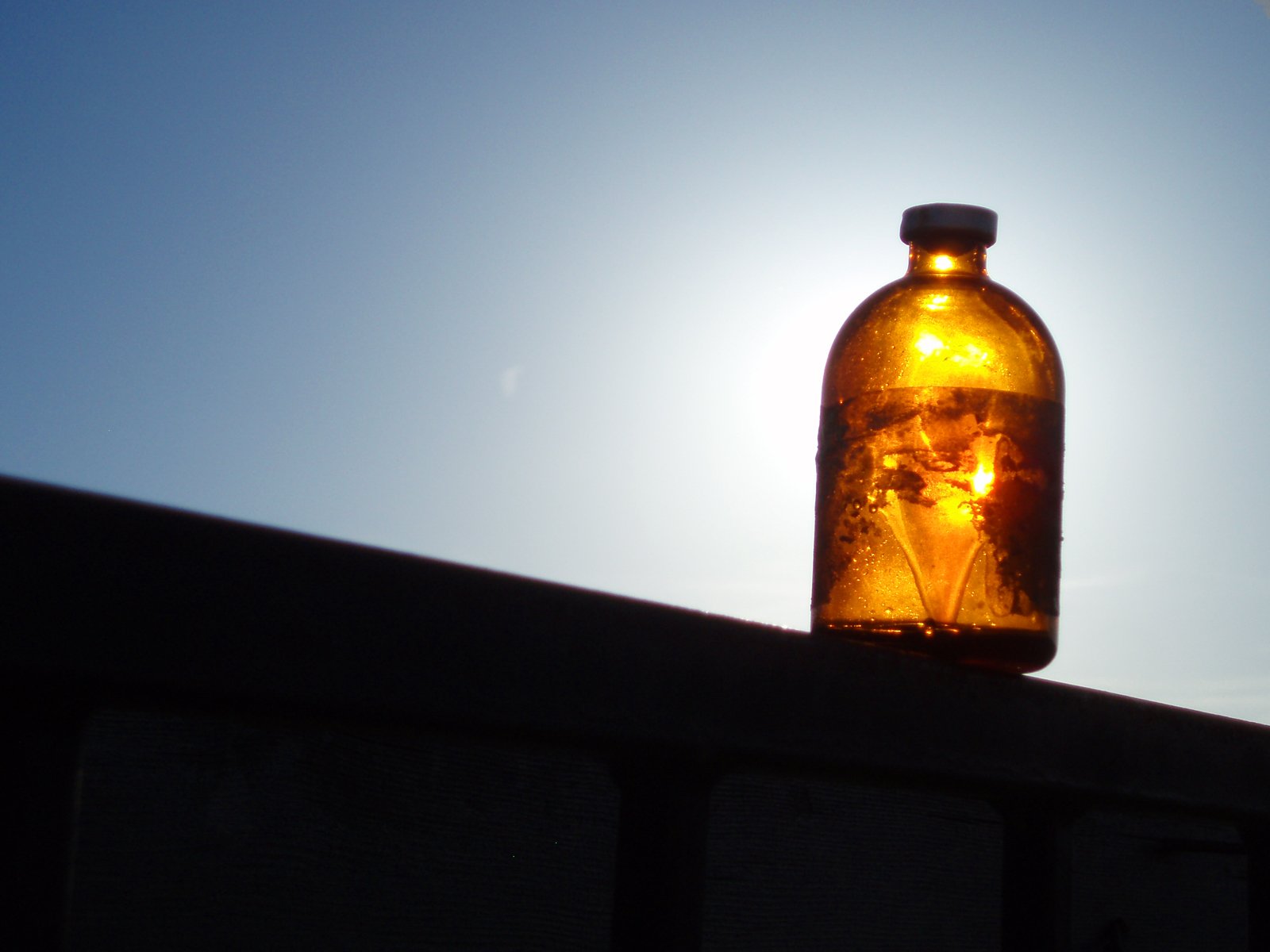 sun shines in front of a brown glass bottle on a metal roof