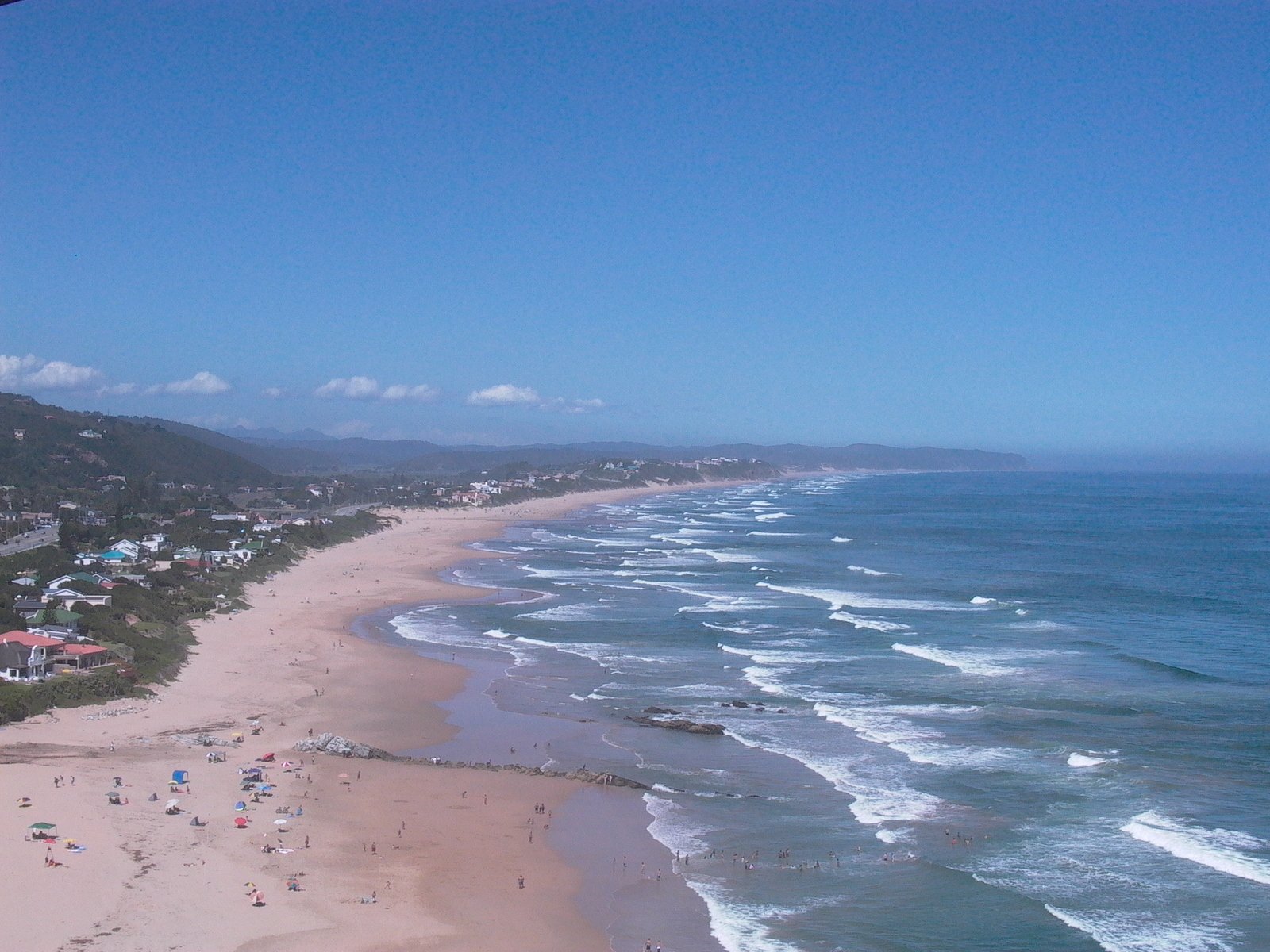 the ocean near the city is quiet with a beach on one side and a lot of people and trees on the other