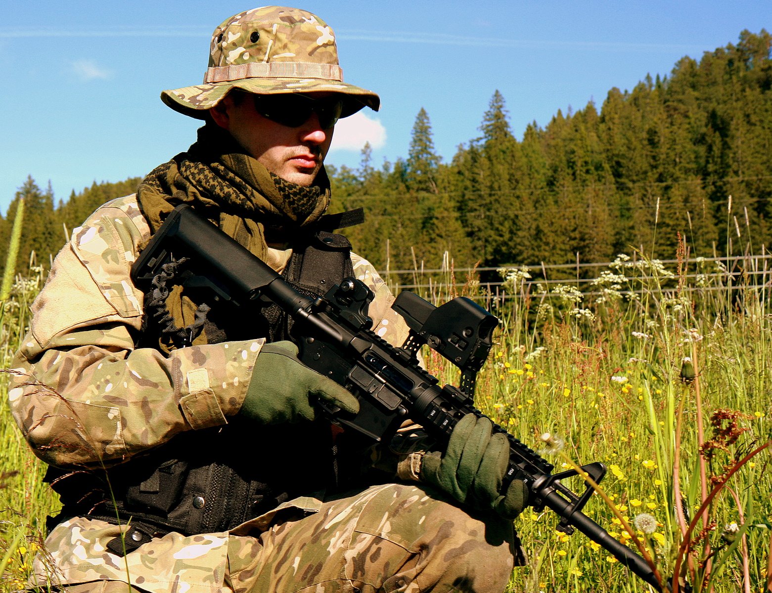 a soldier sitting in the grass with a rifle