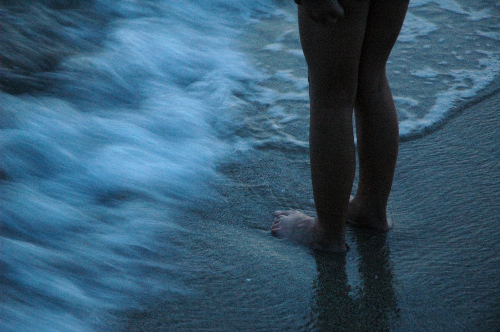 the lower portion of a woman's legs and feet, against a background of dark blue water and foam