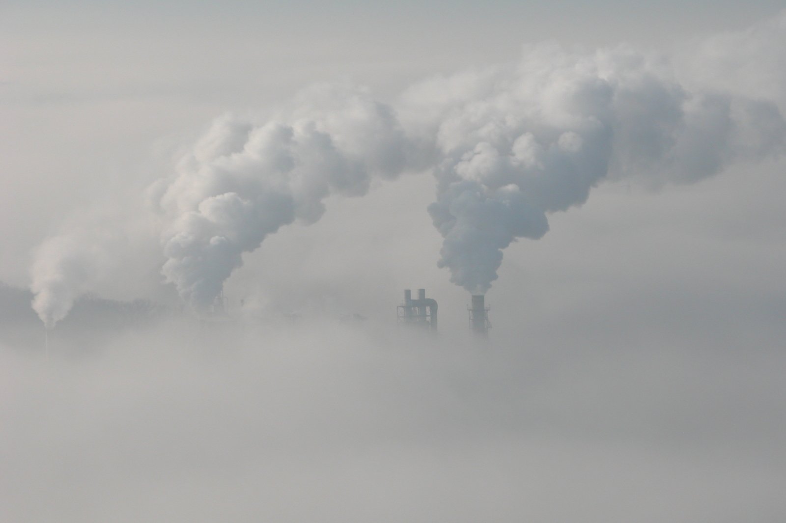 smoke stacks from industrial smokestacks rise above clouds in the sky
