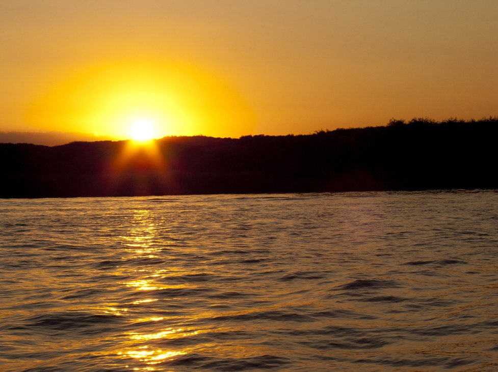 a small boat floats through the water as the sun sets